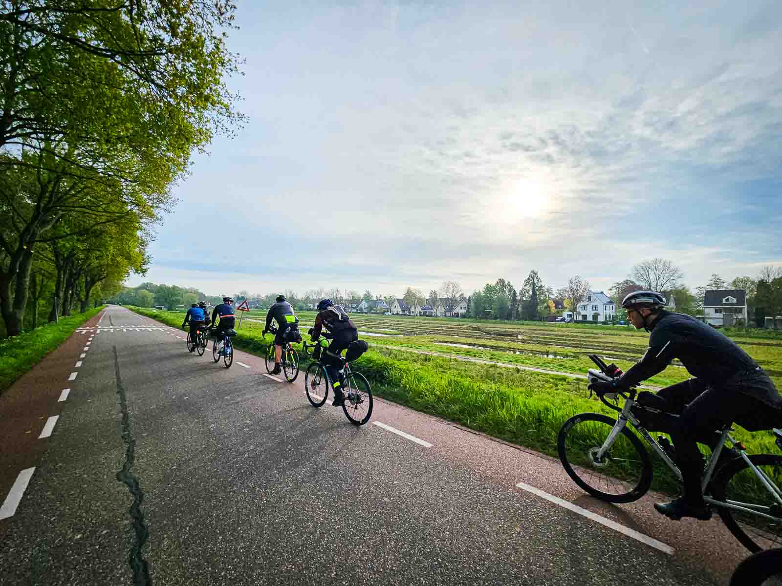 Diversi ciclisti pedalano l'uno dietro l'altro su una strada della Corsa intorno ai Paesi Bassi