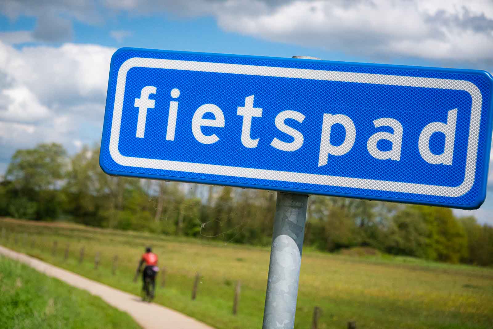 In primo piano, un cartello con la scritta “Fahrradweg” (pista ciclabile) e, fuori fuoco, un ciclista sulla pista ciclabile sottostante.