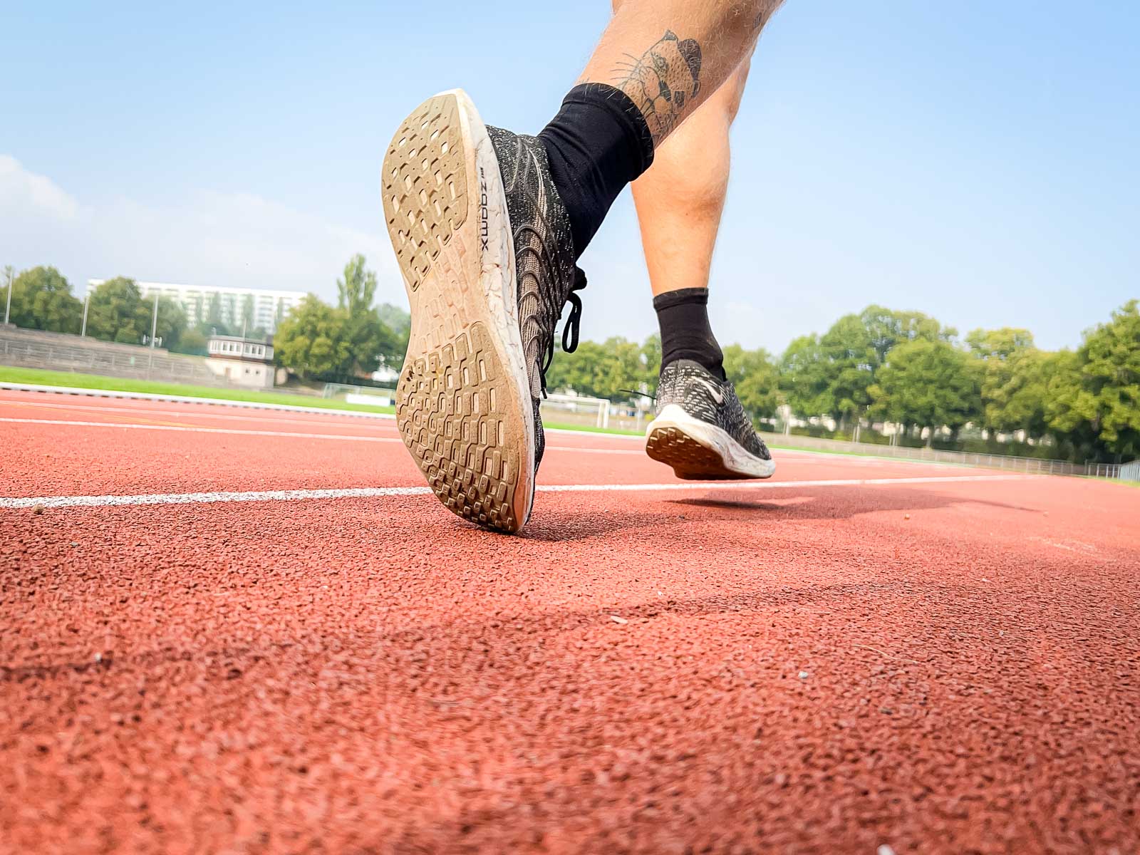 Primo piano delle scarpe di un corridore sulla pista rossa, pronto per l'allenamento. La scena simboleggia determinazione e concentrazione atletica.