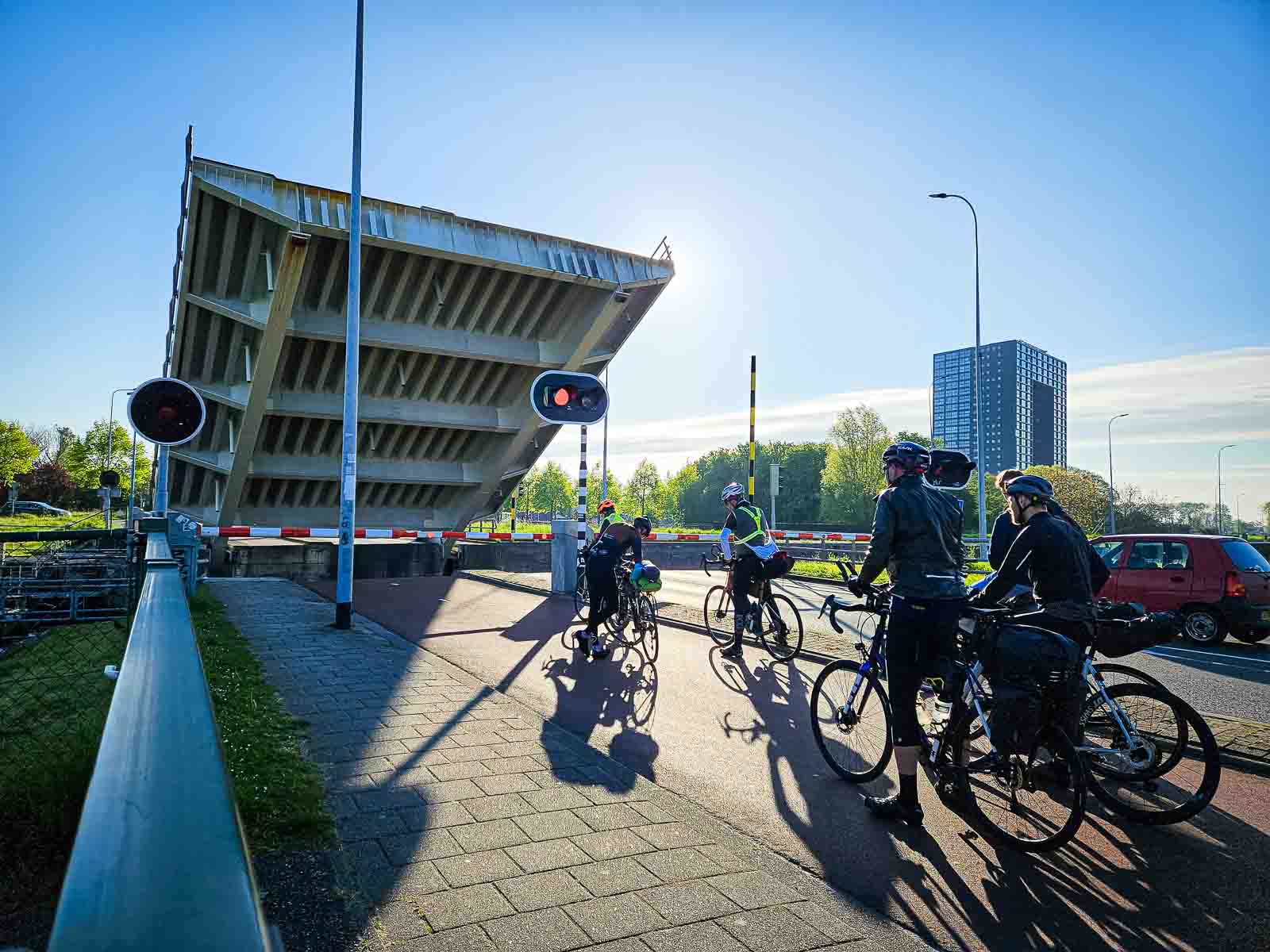 Vari partecipanti alla Corsa intorno ai Paesi Bassi sono in attesa presso un ponte sopraelevato.