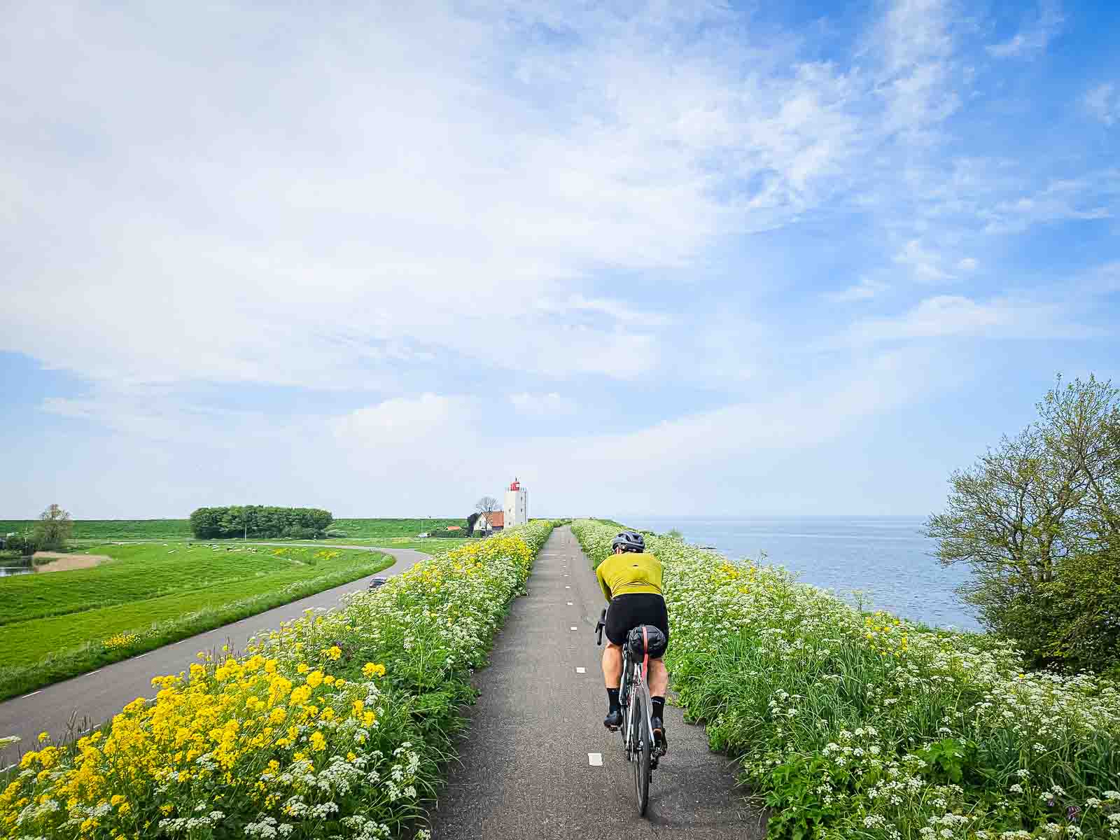 Un ciclista percorre una bella pista ciclabile vicino al mare, in direzione di un faro