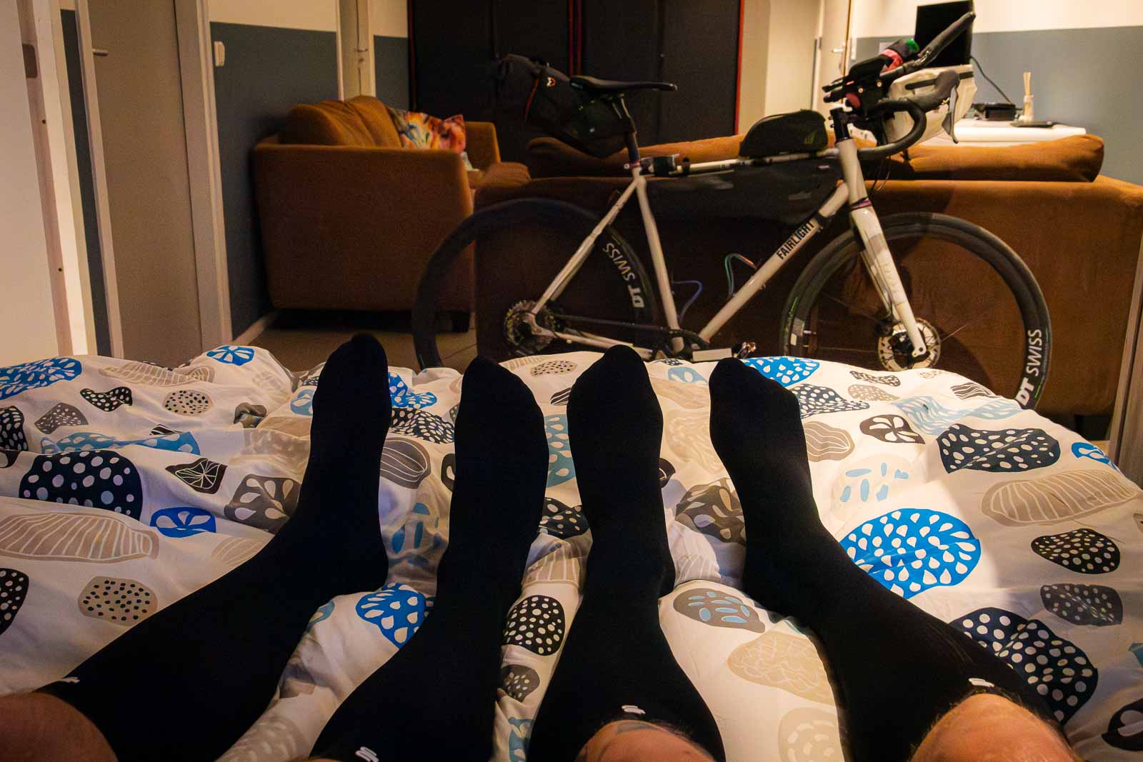 Due partecipanti alla Race around the Netherlands si sdraiano a letto indossando calzini di recupero dopo una giornata faticosa.