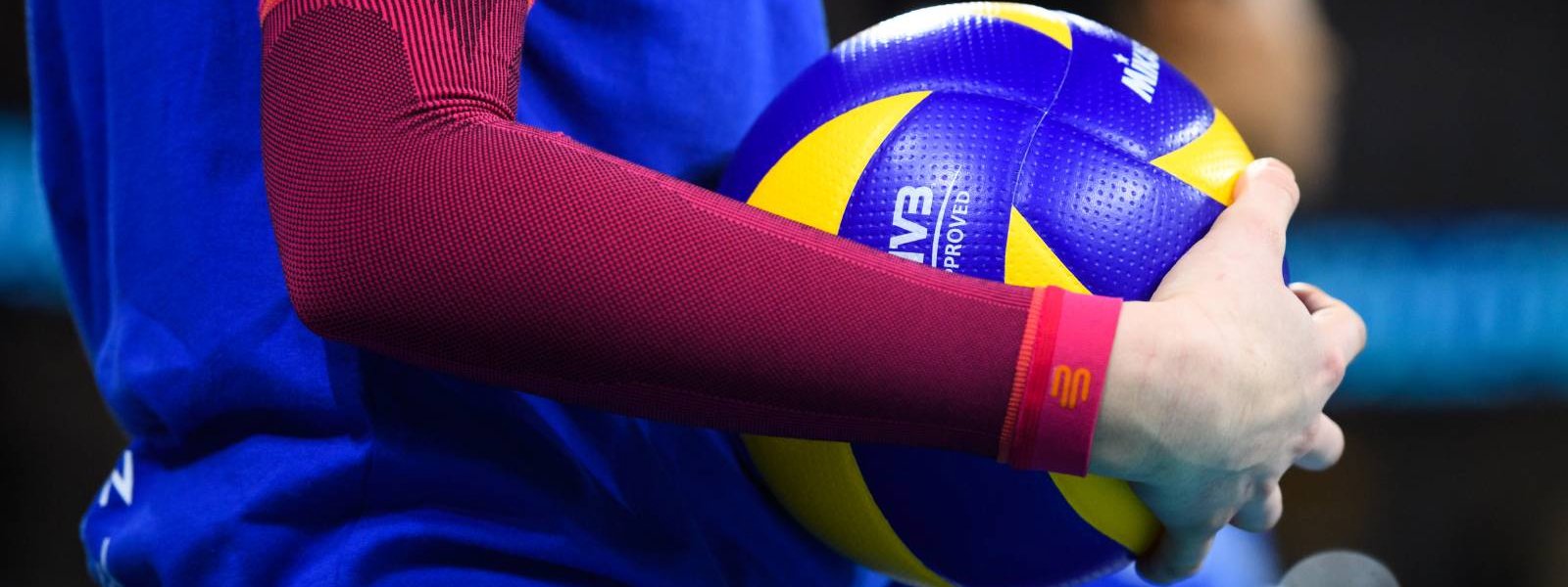 Il giocatore di pallavolo con maniche a braccio rosa ha una pallavolo in mano