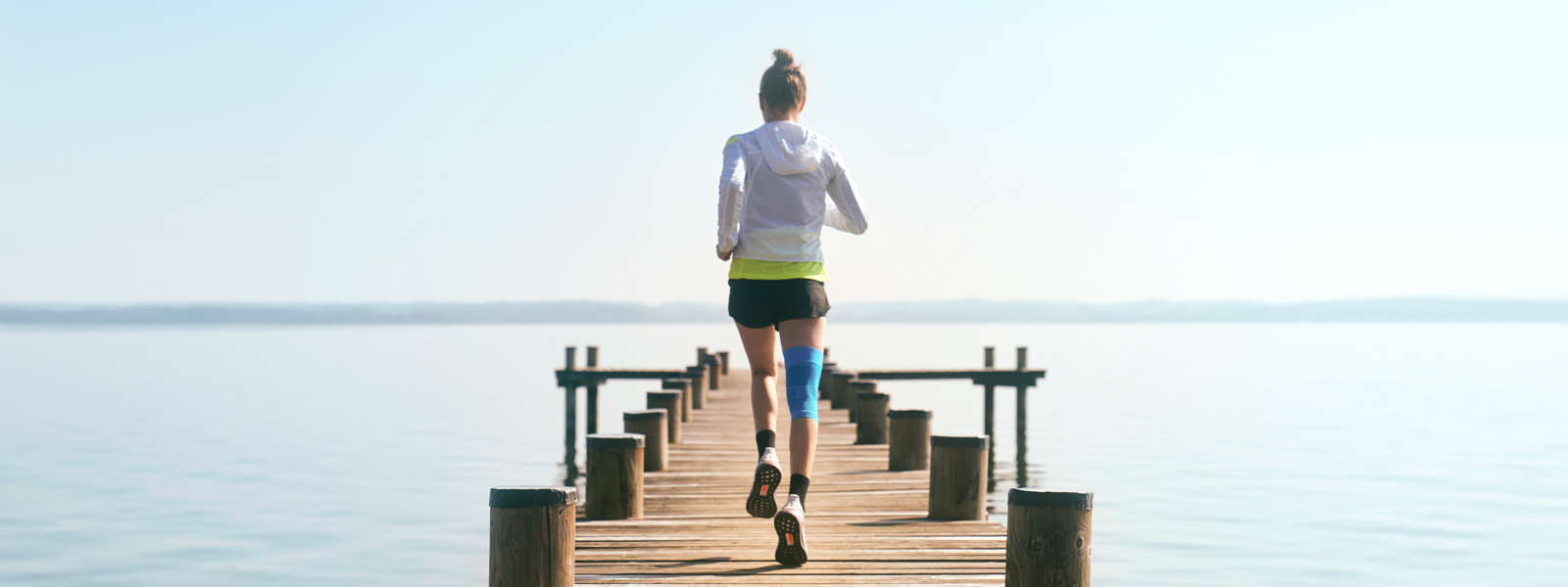 Anna Hahner corre con il suo supporto per il ginocchio di compressione sportiva tramite un molo verso il lago