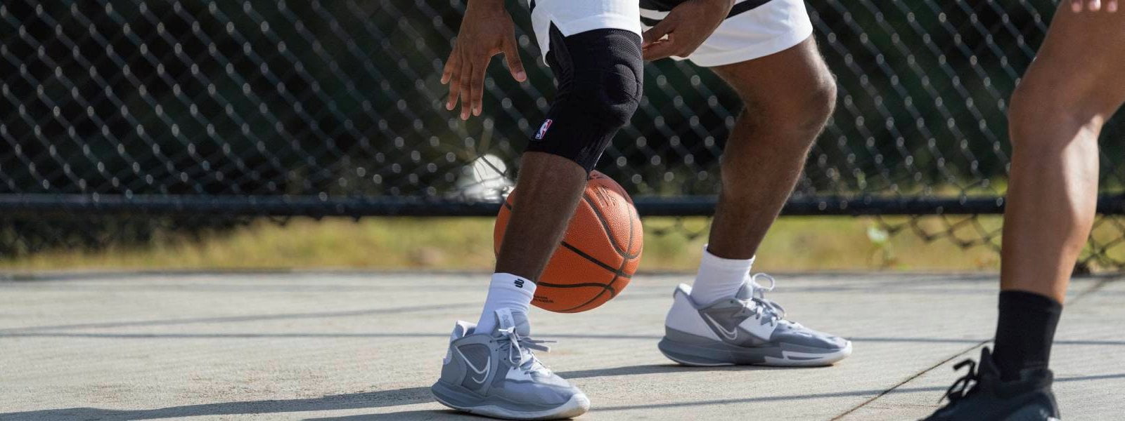 Il giocatore dribba su un campo da streetball con un basket e indossa un supporto per il ginocchio NBA nero