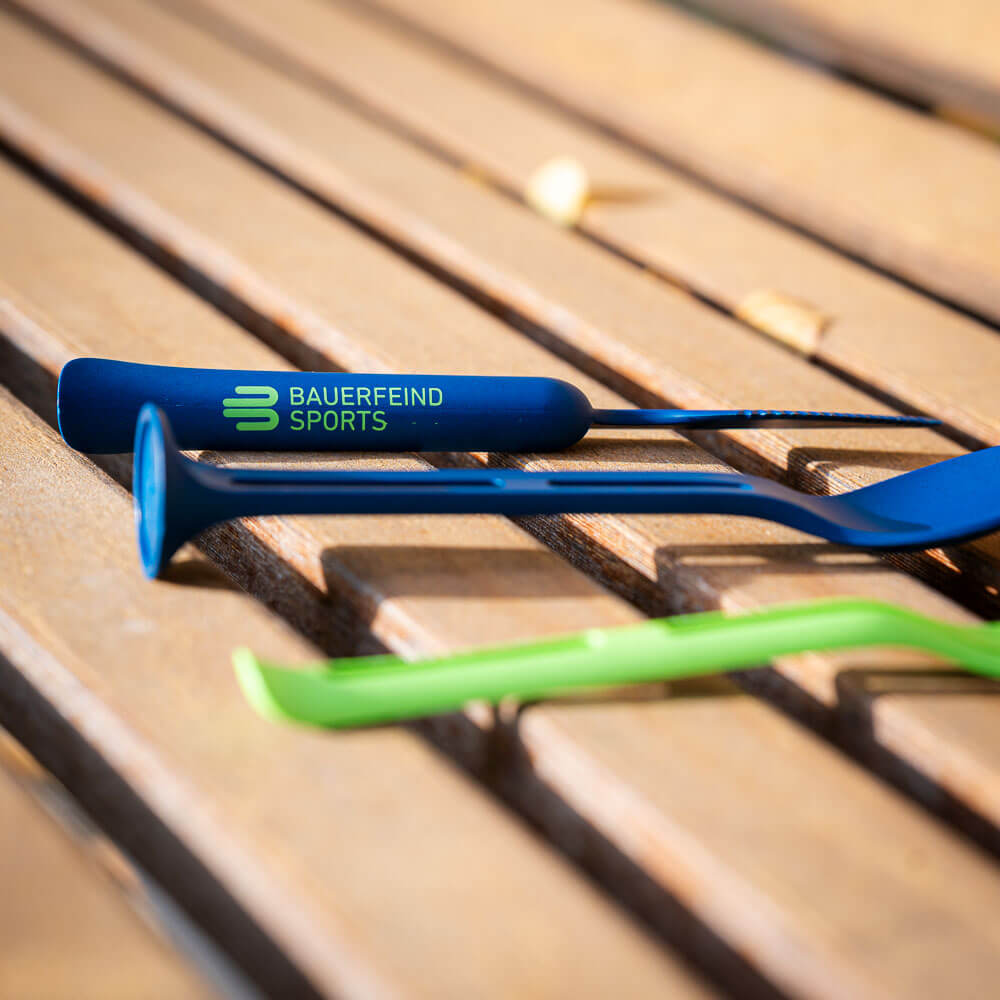 Primo piano di una posata blu su una panchina di legno, con il logo "Bauerfeind Sports" visibile sul manico.