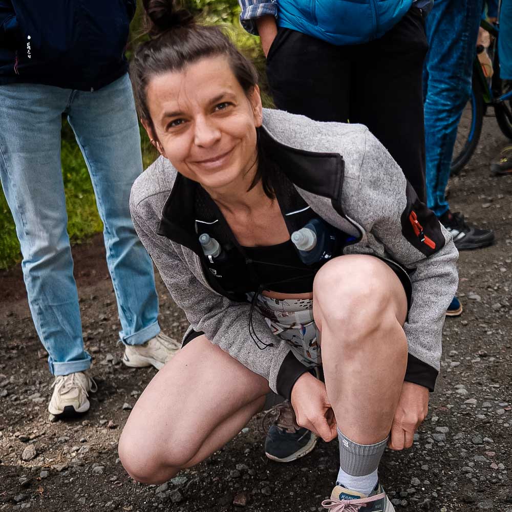 Una donna sorride alla macchina fotografica mentre si aggiusta i calzini da trail running di media lunghezza