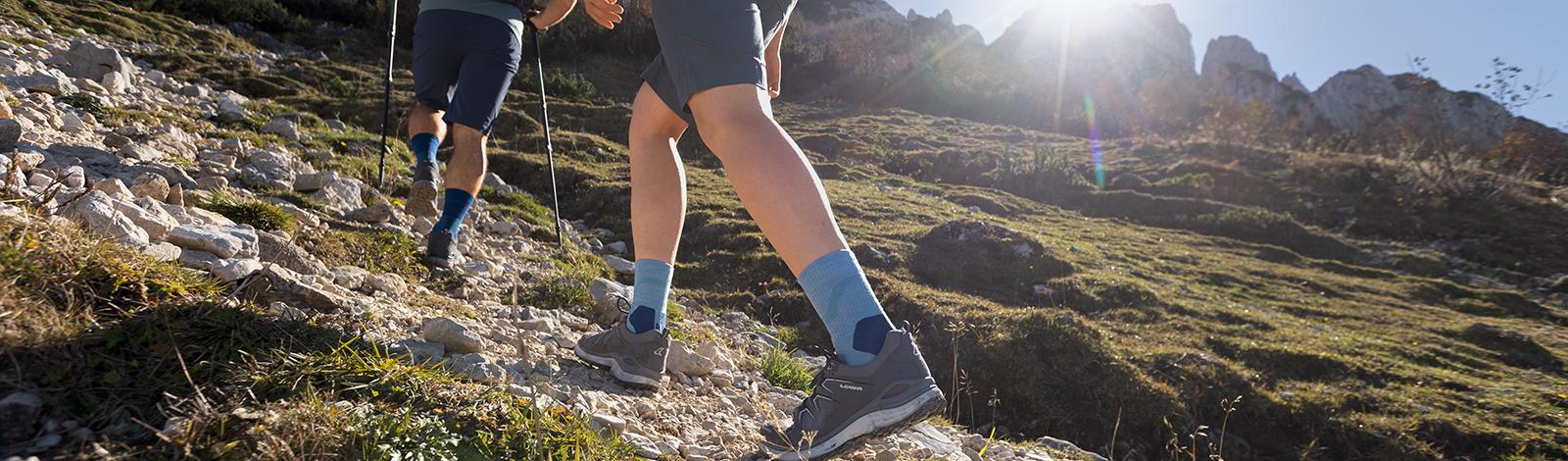 Due escursionisti con calzini da trekking blu di media lunghezza percorri un sentiero di macerie in un idilliaco paesaggio di montagna verde