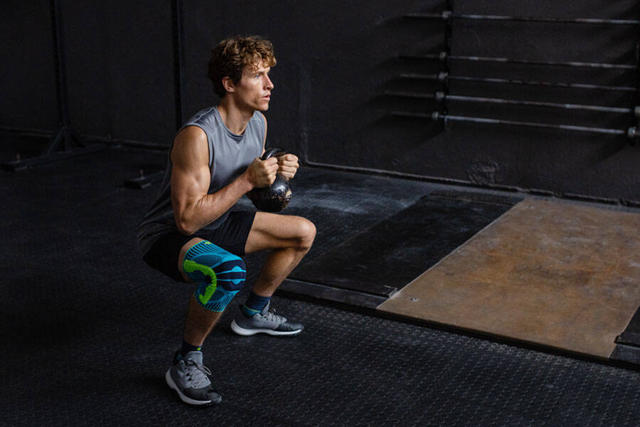 L'uomo con un ginocchio va profondamente accovacciato con un kettlebell tra le due mani