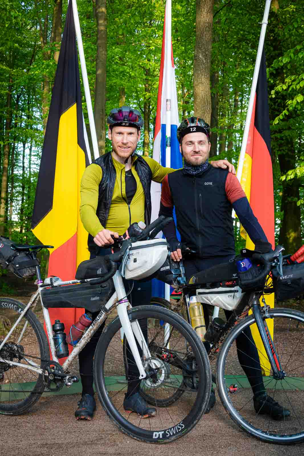 Due ciclisti si trovano al triangolo di confine tra Germania, Belgio e Paesi Bassi e ridono davanti alla telecamera.