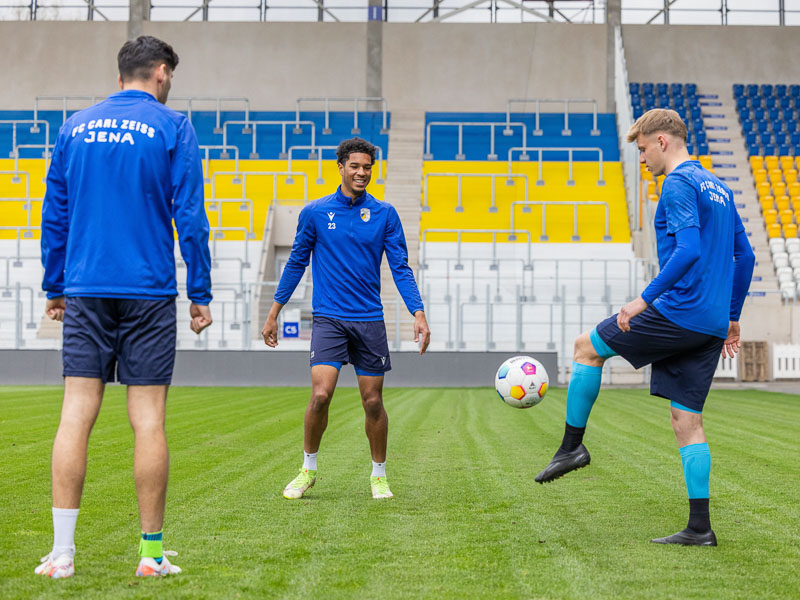 Tre giocatori del FC Carl Zeiss Jena allo stadio durante l'allenamento con un pallone da calcio, che indossano vari prodotti Bauerfeind Sports