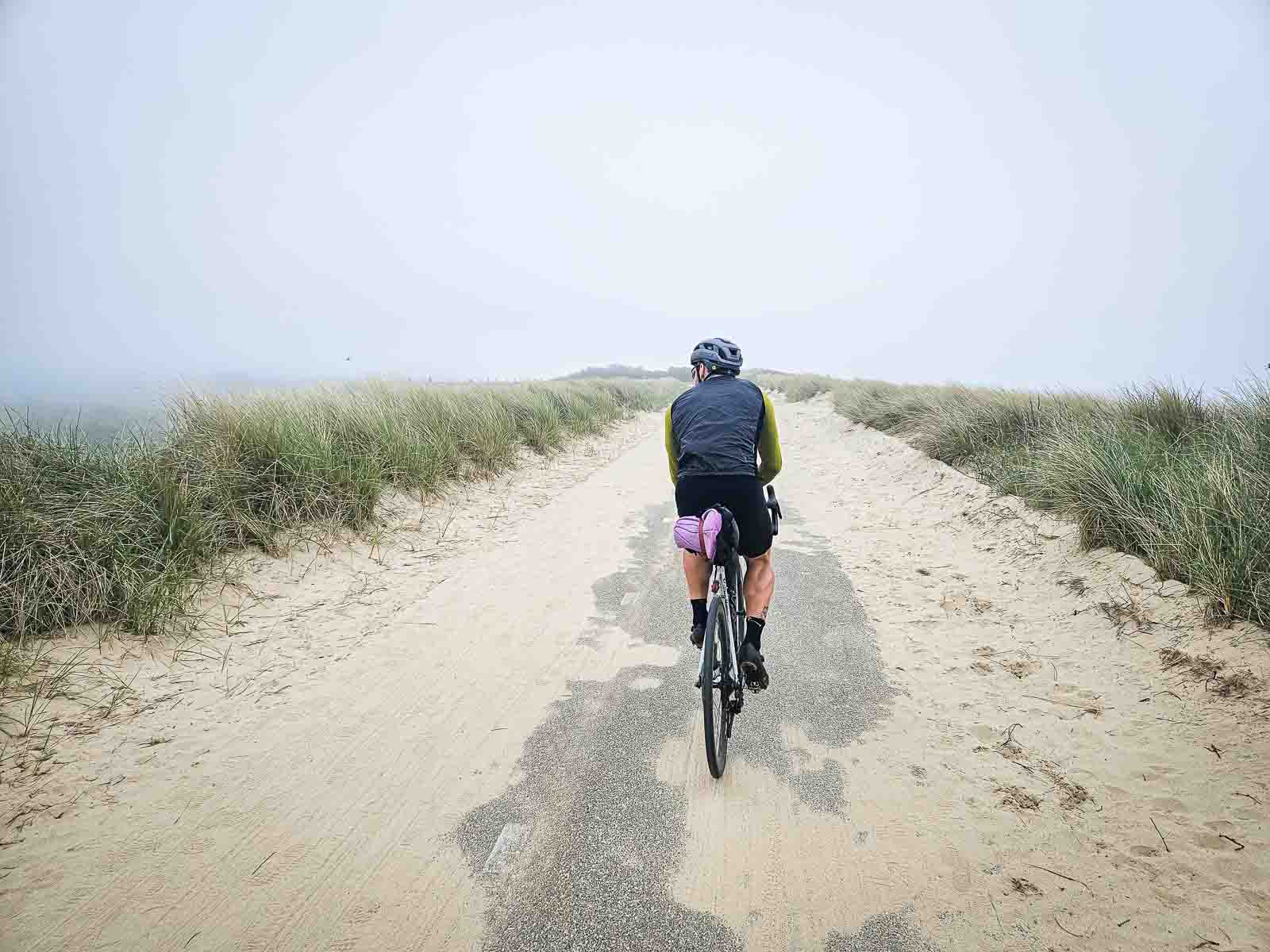 Un ciclista percorre una bella strada di dune parzialmente ricoperta di sabbia.